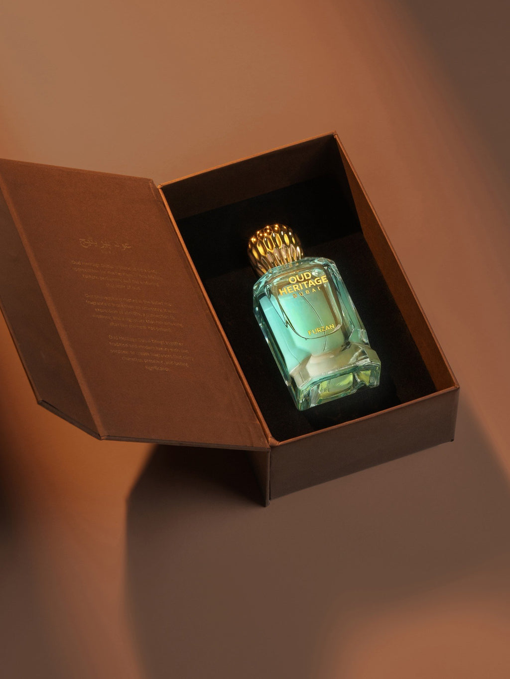 A clear glass perfume bottle filled with light aqua liquid, set inside an open dark brown presentation box with a gold cap, photographed against a warm brown background.