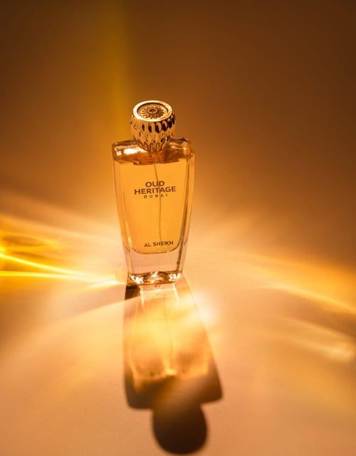 A bottle of Hermès Intense Parfum centered on a warm golden background with dramatic light streaks and a reflection below. The black phone app interface borders are visible around the screenshot.